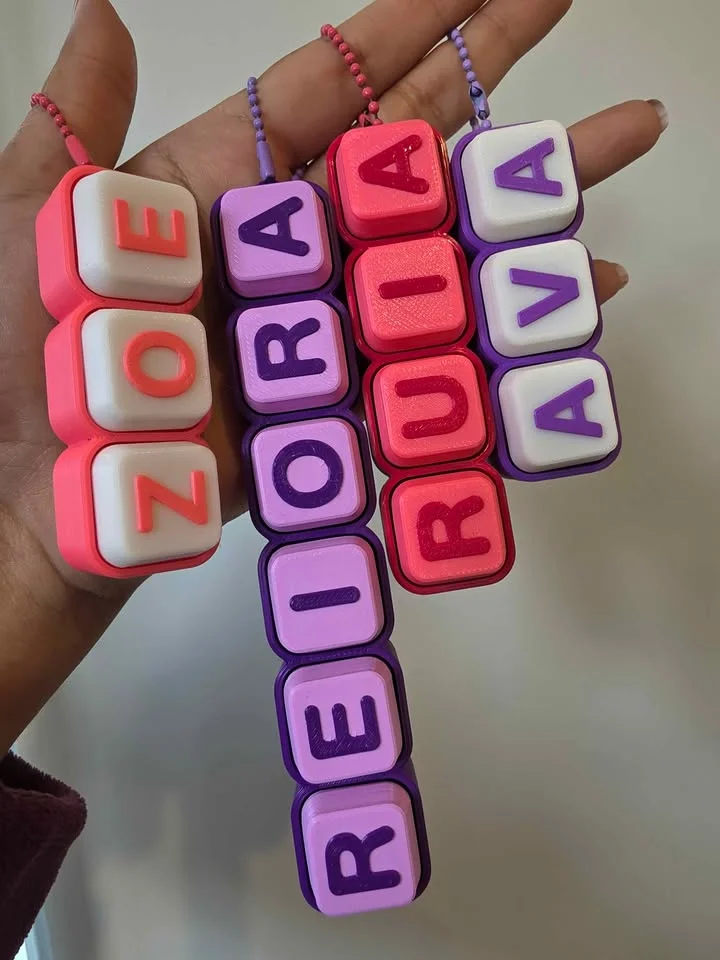 A hand holding a bunch of clicky keyboard-key name keychains in red, purple and lilac