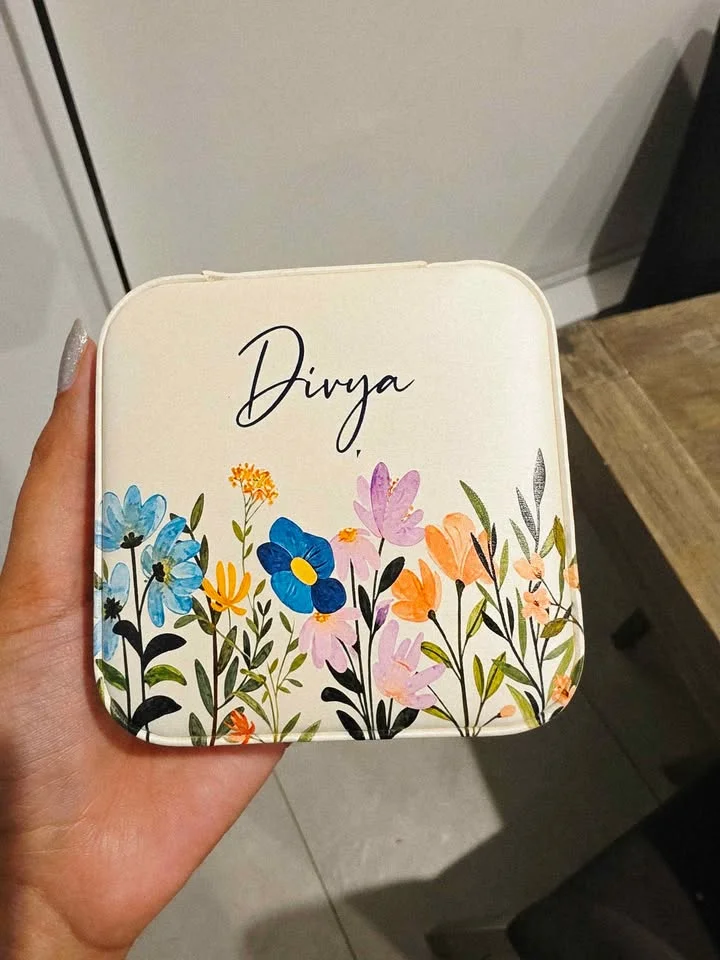 Off-white jewellery box printed with a name in script and a colourful wildflower design, held in a hand
