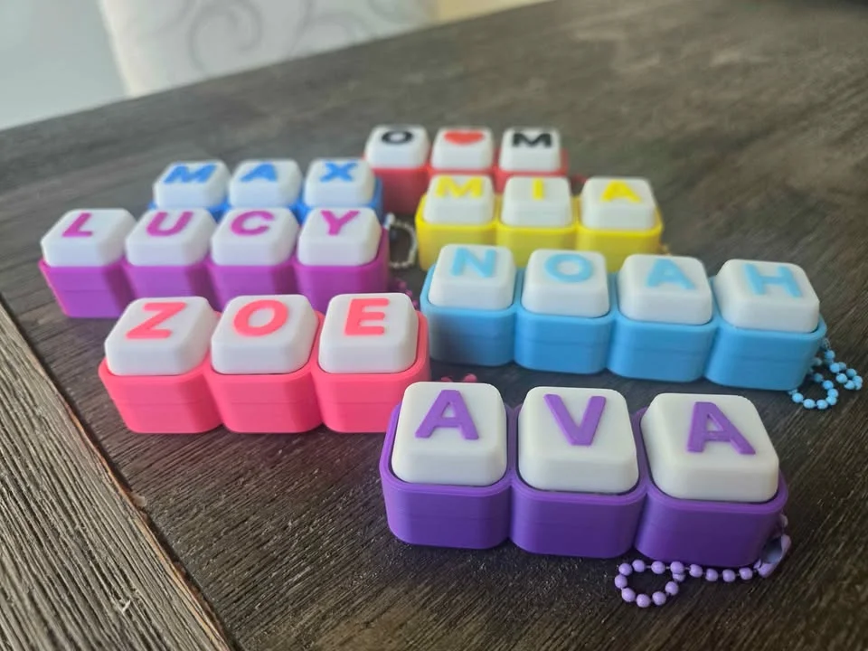 Clicky keyboard-key name tags in pink, light blue, yellow and purple on a table