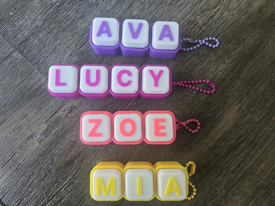 Four clicky keyboard-key name tags in purple, pink, red and yellow with bead chains