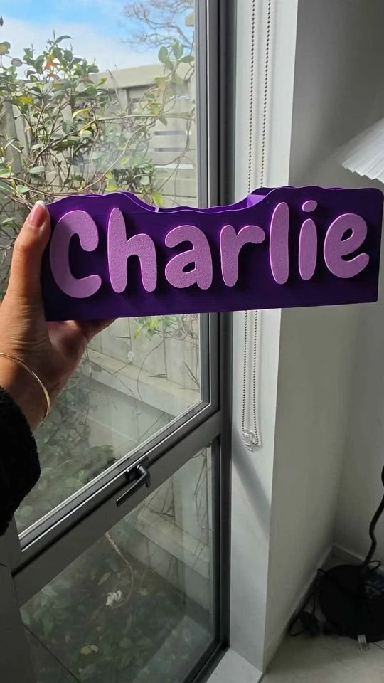 Purple desk organiser with a name in lilac lettering across the front, held up by a window