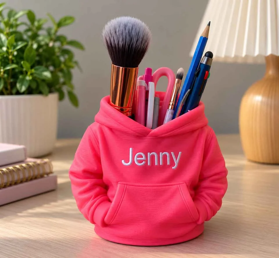 Illustration: hot pink hoodie pencil holder with a white name, holding pens and a brush