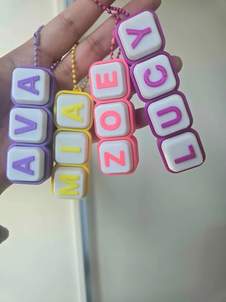 A hand holding four clicky keyboard-key name tags in purple, yellow and pink