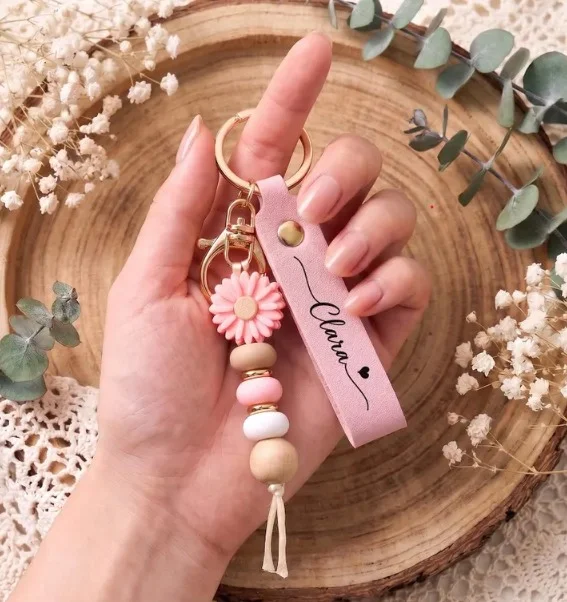Pink name keychain with a daisy charm and wooden beads, held in a hand