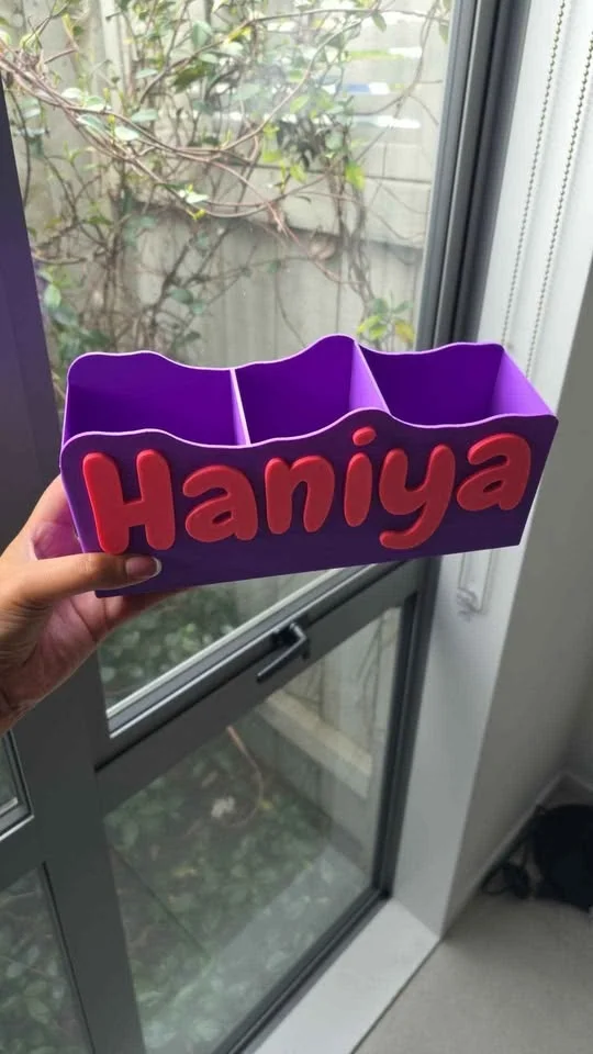 Purple desk organiser with a name in red lettering, held up against a window