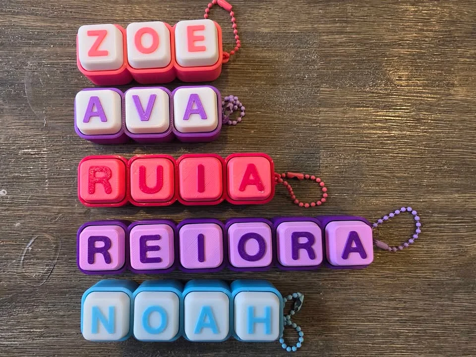 Five clicky keyboard-key name keychains in pink, lilac, red, purple and light blue