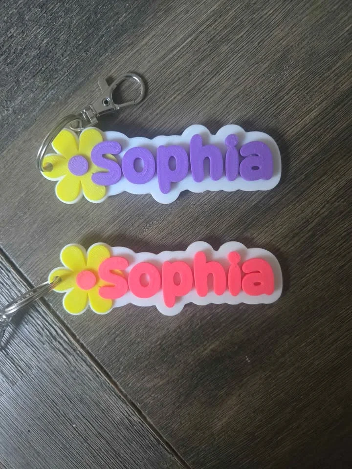 Two 3D printed name bag tags with yellow flowers, one pink and one purple